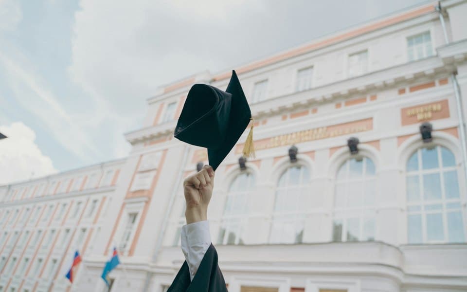 Graduate holding a cap in front of a university building